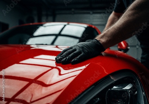 Professional Detailer Polishing Red Sports Car with Protective Gloves in Garage