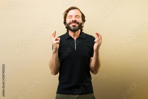 Happy man crossing fingers hoping for good luck and making a wish with eyes closed expressing positive expectation