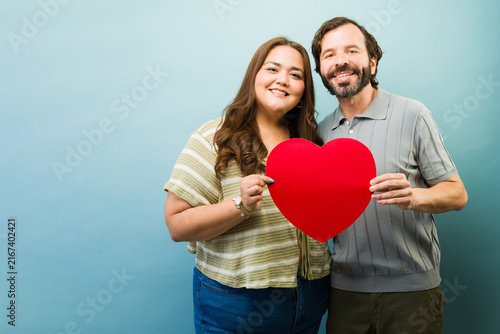 Cheerful couple holding a red heart shape, expressing love and affection on a romantic holiday