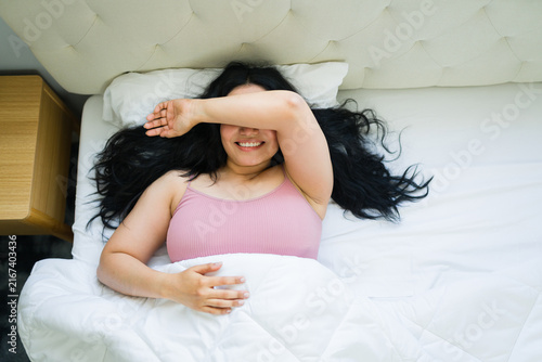 Obraz na płótnie High angle view of a woman waking up in bed covering face with arm, smiling afte