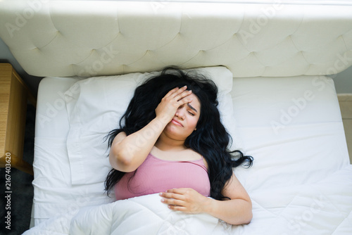 Foto Young woman suffering from a severe headache or migraine in bed, covering her ey