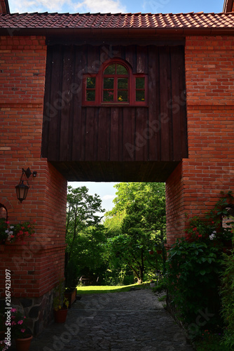 Fotografie A brick arch with a red wooden window with a passage underneath and a view of the lush garden path