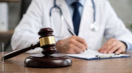 Legal evaluation of medical negligence and medical malpractice lawyer court proceeding featuring a gavel on desk and doctor writing in background.