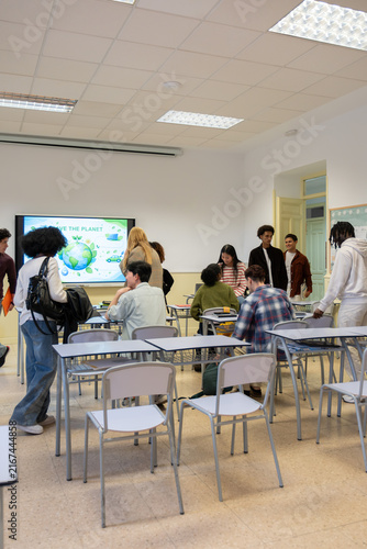 Diverse high school students entering a classroom with an interactive screen displaying an environmental concept