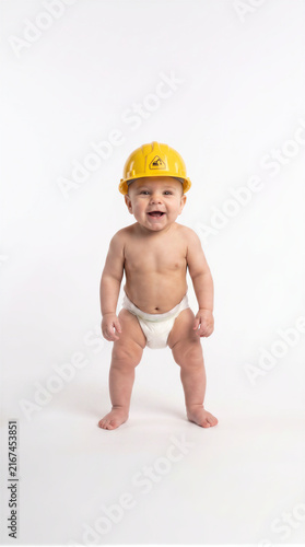 Cute happy baby in diaper wearing yellow construction hard hat standing isolated on background