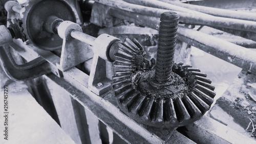 Fotografía Monochrome close-up of an industrial metal gear mechanism with a threaded shaft, grease, pipes, and weathered machinery details creating an engineering texture