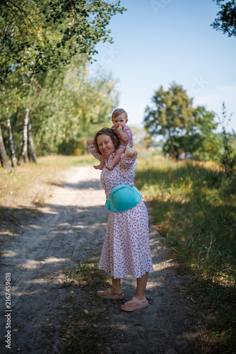 A woman walking along a dirt road with a baby sitting on her shoulders