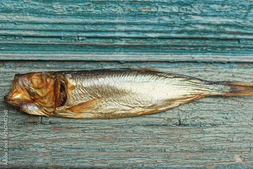 Fotografie one small smoked brown sea fish sprat lies on a green table