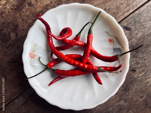 Obraz na płótnie Fresh red chili peppers arranged on a white floral plate over a rustic wooden table, showcasing vibrant color, natural texture, spicy ingredient, and traditional culinary appeal