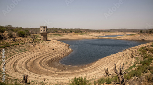 Naklejka Drinking water reservoir at a critically low level with wide bands of cracked exposed shoreline