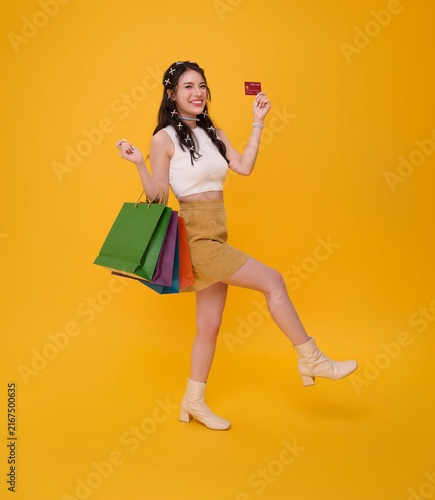 Young woman holding credit card and shopping bags while walking expressing retail shopping cashless payment consumer confidence purchasing power financial freedom and joyful modern lifestyle.