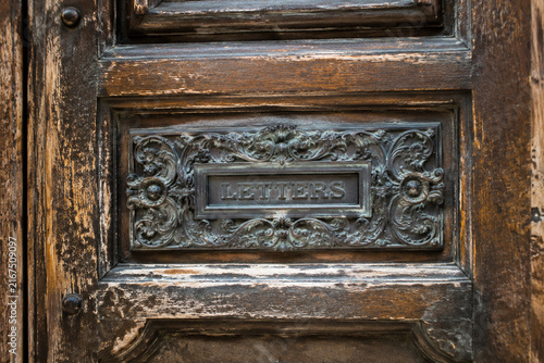 Aged wooden door with an ornate metal plaque inset in the center.