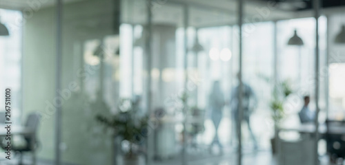 An out-of-focus office interior featuring glass partitions, modern furniture, and blurred figures, emphasizing a collaborative work environment.