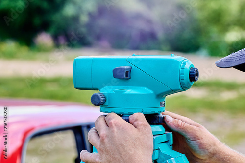 Optical surveying device is positioned on sturdy tripod while user rotates adjustment knobs to prepare precise leveling measurements for field work.