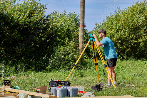 Field specialist uses optical surveying device to measure elevation differences across landscape area.