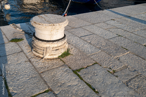 Fotografía Close-up of old stone bollard by water, with dock tiles and sunlight