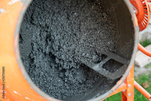 Concrete mixer mixing concrete mortar. Internal view of an orange concrete mixing machine with wet cement and gravel in operation, symbolizing the construction process and material production
