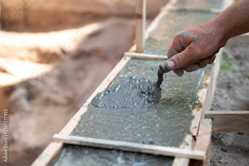Builder smoothing concrete with a trowel in wooden formwork. A worker's hand dips a trowel into fresh concrete mortar inside formwork, symbolizing the foundation construction process