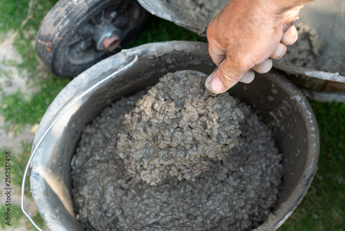 Worker scooping concrete from a bucket with a trowel. Close-up of a hand with a tool and concrete mortar in a bucket, symbolizing hard labor, construction, and the repair process