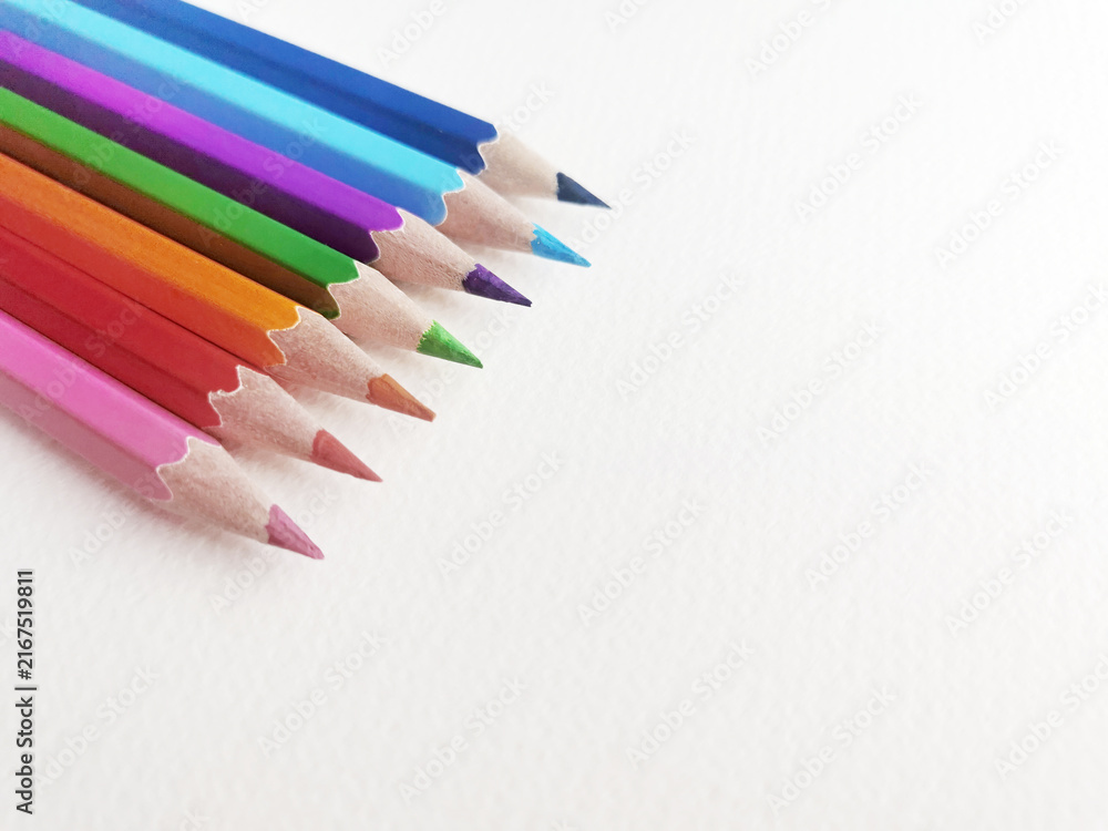 Fototapeta premium Colored pencils lined at angle on white textured paper surface