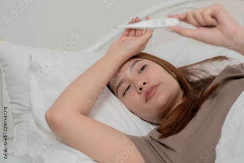 фотографія Fever and illness concept of a sick young woman lying in bed and checking her te