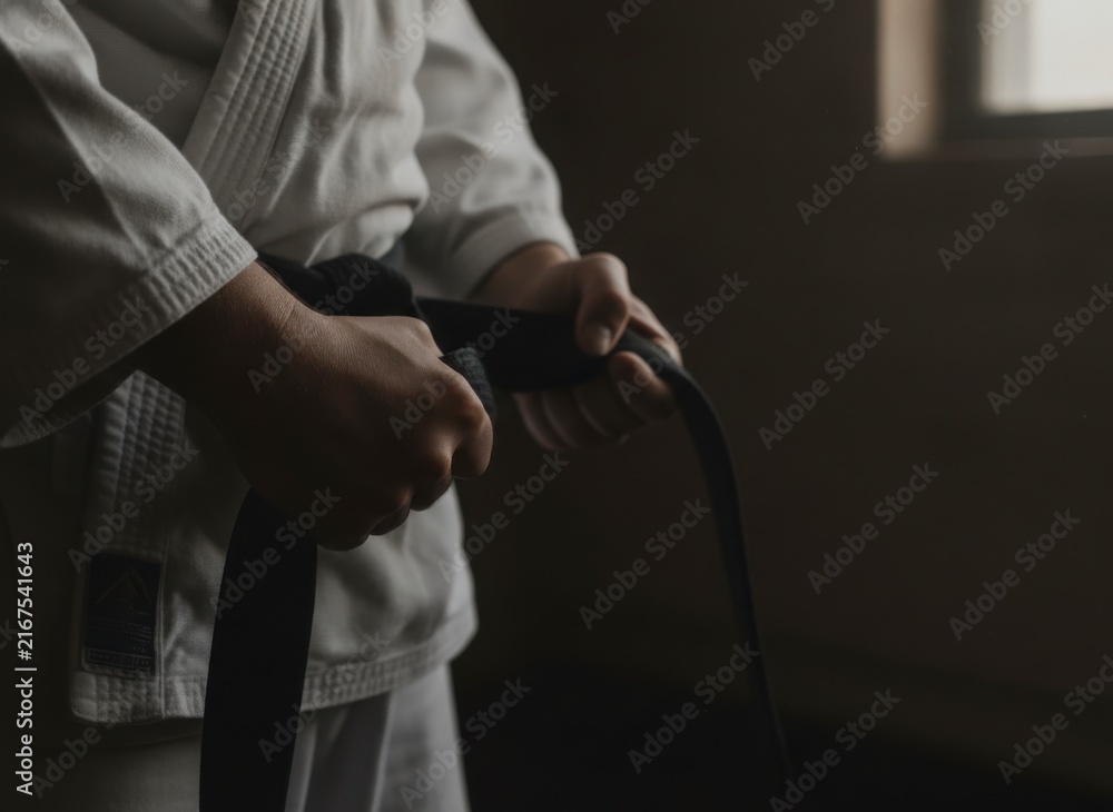 Naklejka premium Close-up of a person's hands tying a black belt on a white martial arts uniform