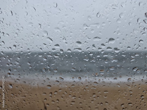 Foto Full frame view of water droplets clinging to a glass window with a blurred view of a stormy sea and beach in the background under an overcast sky