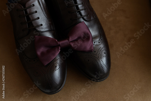 Photography Brown leather wingtip brogue shoes with burgundy bow tie close up, elegant groom wedding accessories, modern classic gentleman style