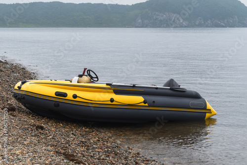  Yellow inflatable motorboat on rocky seashore with calm sea and forested coastal hills.