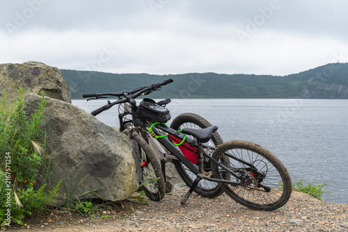  Mountain bikes resting on rocky seashore with calm sea and forested hills. bike rides in nature, healthy lifestyle.