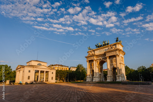 Arco della Pace monument in Milan, Italy, surrounded by green trees and a clear blue sky during golden hour lighting