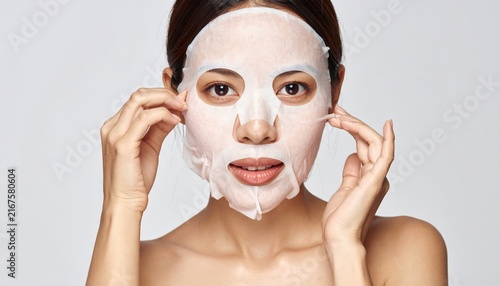 Woman applying sheet mask carefully to face, skincare routine concept, clean background