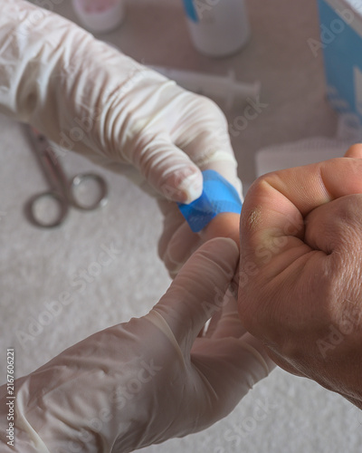 Close-up of gloved hands applying a bandage to a finger after a minor cut. First aid supplies like medical tape, scissors, and a kit are visible in the background