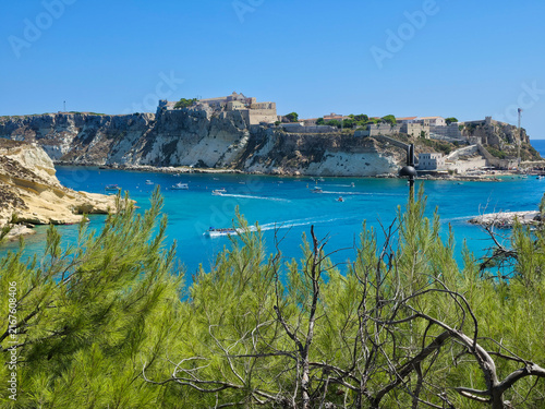 San Nicola Island Fortress and Cretaccio Rock Framed by Green Pine Trees from San Domino, Tremiti Islands, Italy – Turquoise Sea with Moving Boats Under Blue Sky
