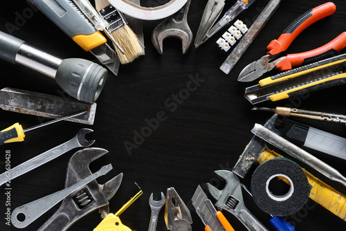 Assorted hand tools and repair supplies arranged around empty center on dark workshop surface