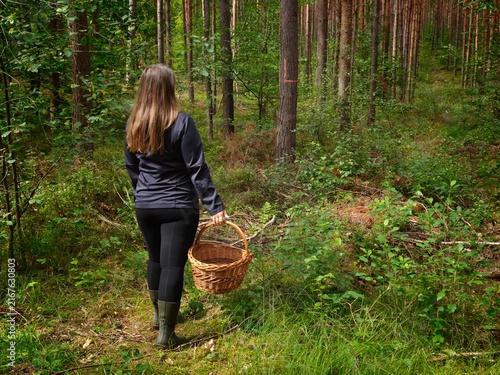 Woman walking through a forest with a wicker basket while foraging for wild mushrooms