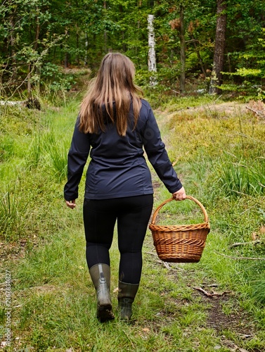 Woman walking through a forest with a wicker basket while foraging for wild mushrooms