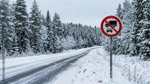 A Red Traffic Prohibitive Symbol Positioned Alongside an Ice Covered Rural Highway Surrounded by Dense Evergreen Forest Trees During Cold Winter Season road sign winter snow transport traffic