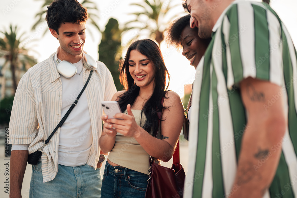 Obraz premium Group of diverse friends sharing happy moments and connecting using a smartphone outdoors in a city street