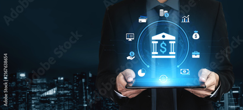 Digital Banking Concept with a Businessman Holding a Tablet Displaying Financial Icons and Virtual Bank Building at Night in a Modern City Environment. Entropy.