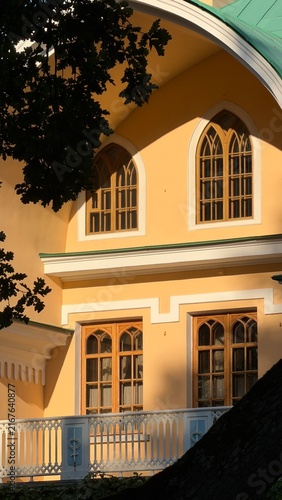 Fotografie Sunlit facade of a yellow classic building featuring gothic-style arched wooden windows and a white balcony