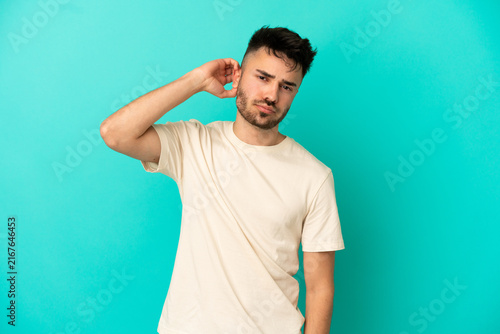 Obraz na płótnie Young caucasian man isolated on blue background having doubts
