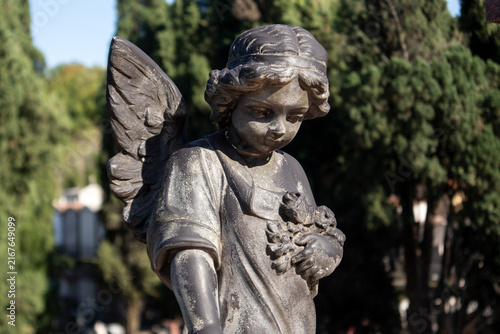 Принти на полотні Antica statua di angelo custode con ali e fiori in un cimitero storico, scultura
