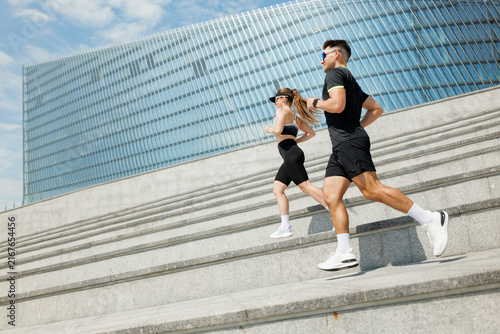 Картината върху платно Running duo navigating steps with energy in a modern urban landscape under a bri