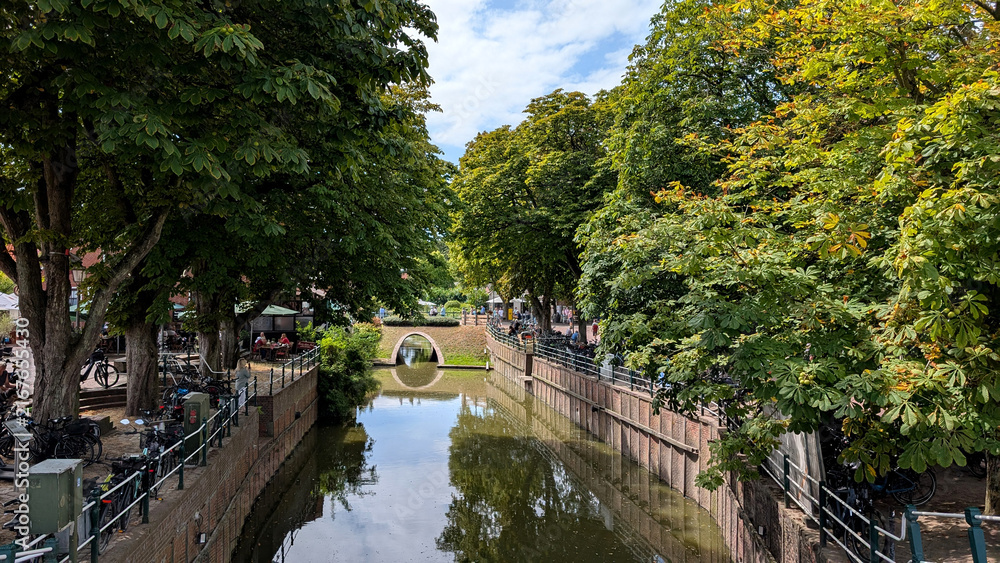 Fototapeta premium Tree-lined canal with small bridge in Greetsiel, Germany. 