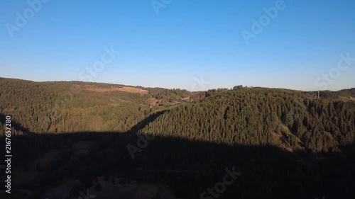 Peaceful aerial drone view over lush green forests and rural countryside on a clear summer morning, with scattered houses, winding roads and natural landscape.