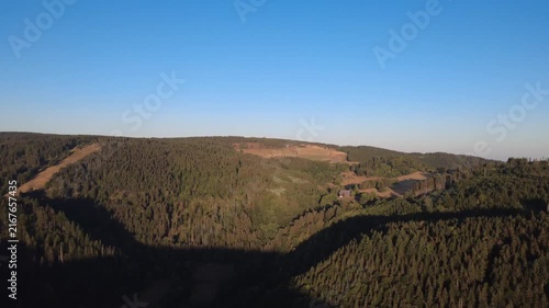 Peaceful aerial drone view over lush green forests and rural countryside on a clear summer morning, with scattered houses, winding roads and natural landscape.