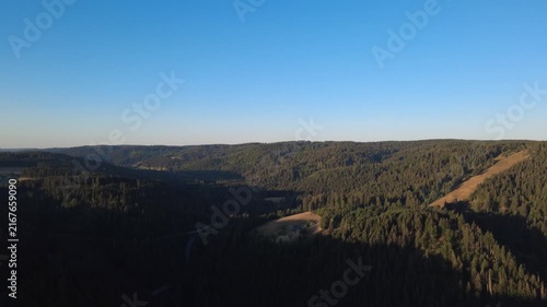 Peaceful aerial drone view over lush green forests and rural countryside on a clear summer morning, with scattered houses, winding roads and natural landscape.