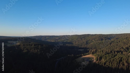 Peaceful aerial drone view over lush green forests and rural countryside on a clear summer morning, with scattered houses, winding roads and natural landscape.