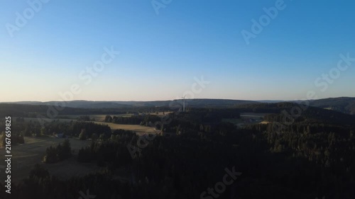 Peaceful aerial drone view over lush green forests and rural countryside on a clear summer morning, with scattered houses, winding roads and natural landscape.